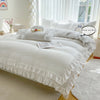 A white ruffled duvet cover set displayed on a bed with sheer white curtains and natural light.