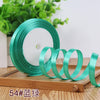 Roll of satin ribbon in teal green color resting on a wooden surface.