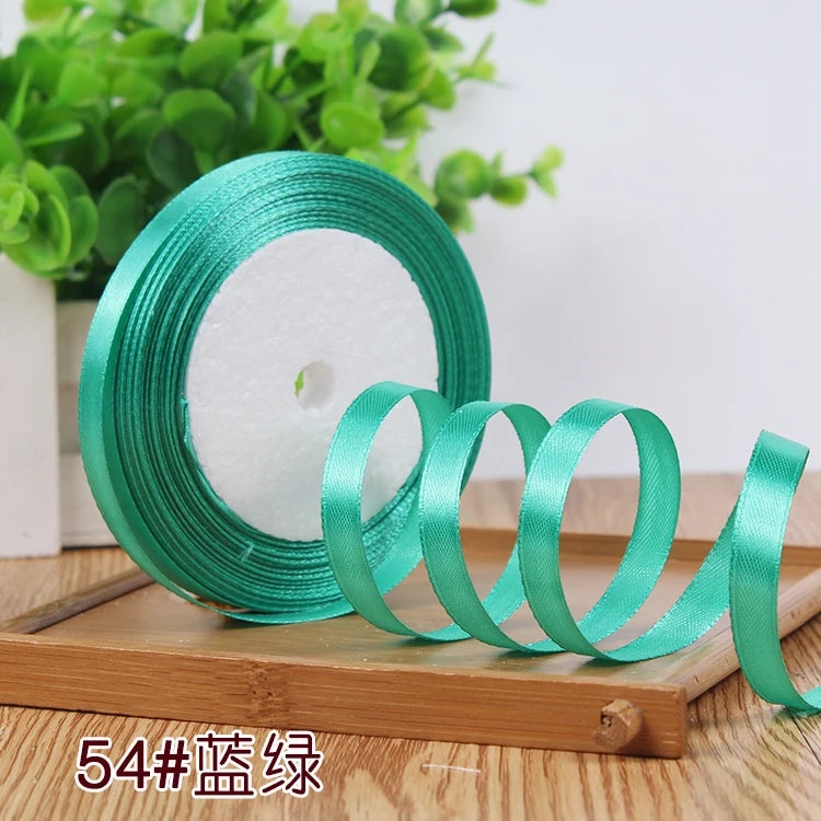 Roll of satin ribbon in teal green color resting on a wooden surface.