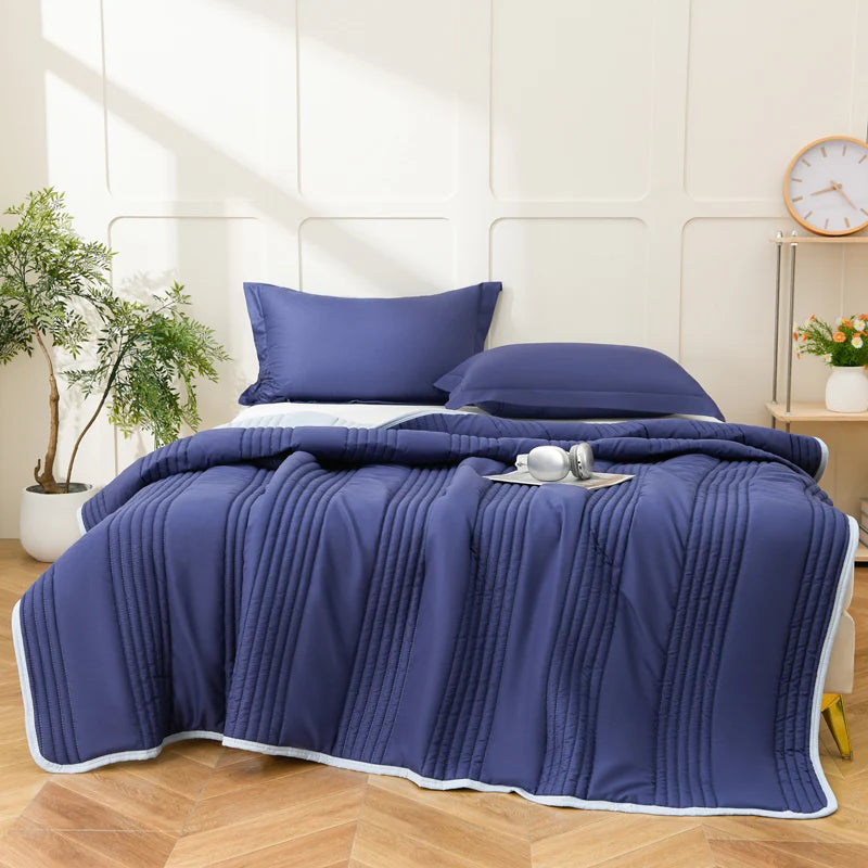 A navy blue lightweight quilted summer blanket is draped over a bed, featuring vertical pleats.
