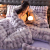A woman is relaxing under a fluffy gray plush rabbit hair bedding set on a bed.