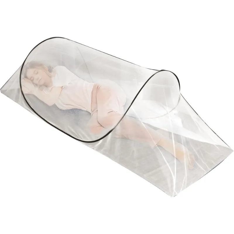 A person lying down inside a clear, portable mosquito net pop-up bed for camping or travel.