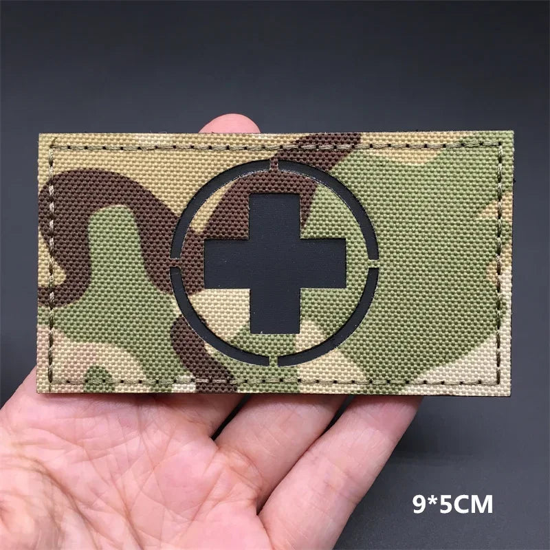 A tactical patch featuring a medical cross symbol on a camouflage fabric background.