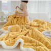 A thick yellow fleece blanket with white trim is draped on a bed, shown from the back.