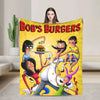 A colorful throw blanket featuring a cartoon illustration of a family preparing burgers.