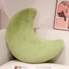A light green moon-shaped throw pillow resting on a white surface.