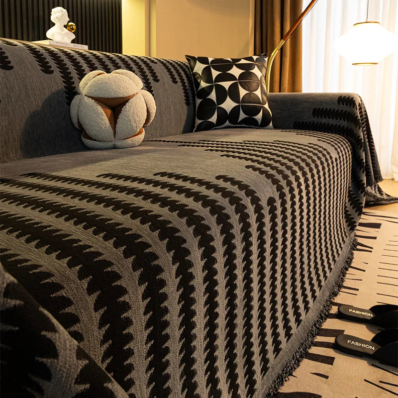 A close-up of a charcoal gray herringbone chenille sofa cover with black geometric patterns and tassel fringes.
