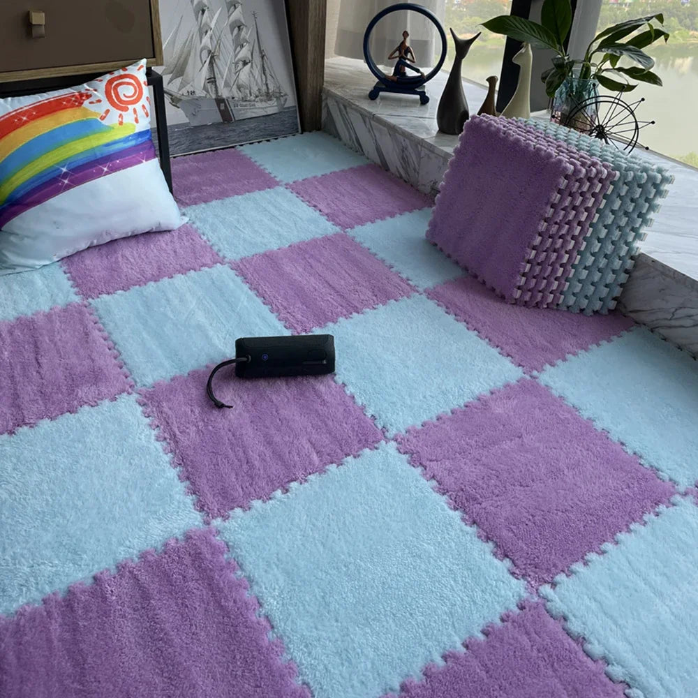 A pink and blue checkered soft plush EVA foam play mat with a purple pillow and a black electronic device on the floor.