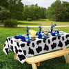 A table set for an outdoor event featuring a black and white cow print tablecloth with blue and yellow food items.
