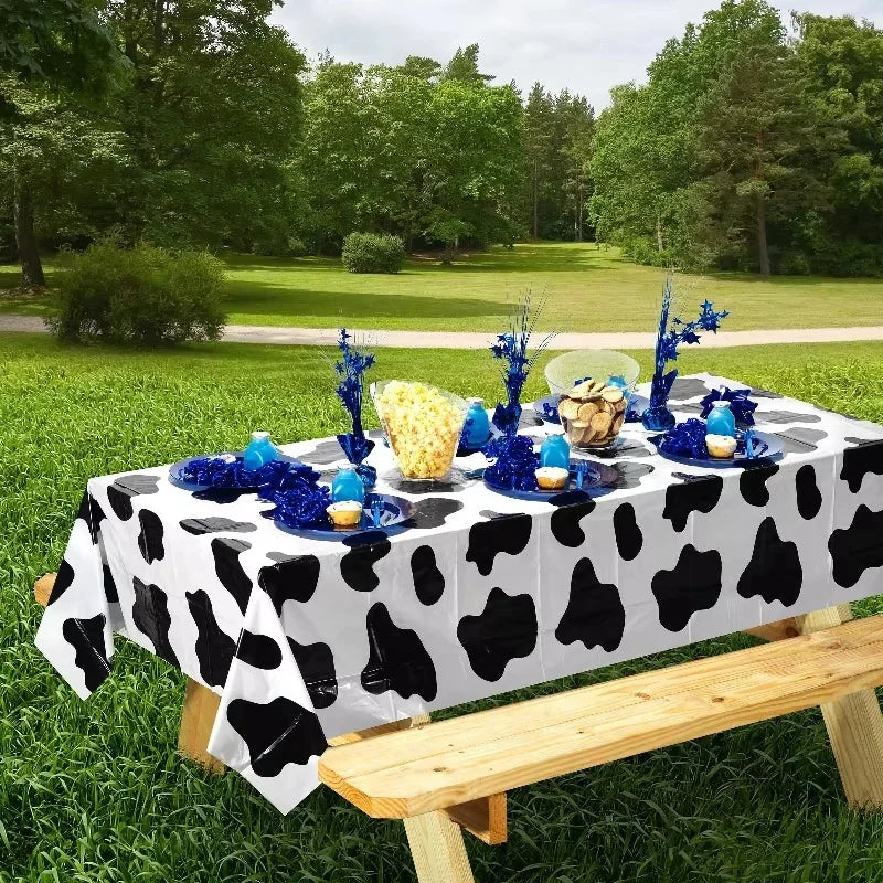A table set for an outdoor event featuring a black and white cow print tablecloth with blue and yellow food items.