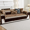 A brown and gold patterned quilted sofa cover with decorative trim and accent pillows on a white sofa.