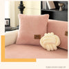 A pink sherpa sofa cover with a cream knitted decorative pillow and a yellow accent box.