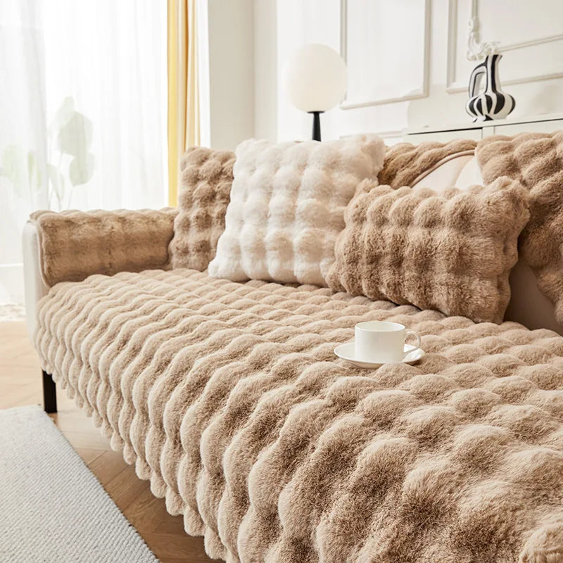 A beige plush rabbit fur sofa cushion cover draped over a sofa with light curtains and white decor.