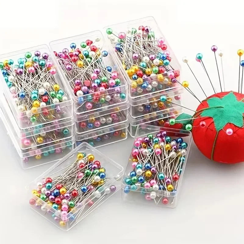 Clear plastic containers filled with assorted colorful sewing and pinning needles arranged around a red strawberry.