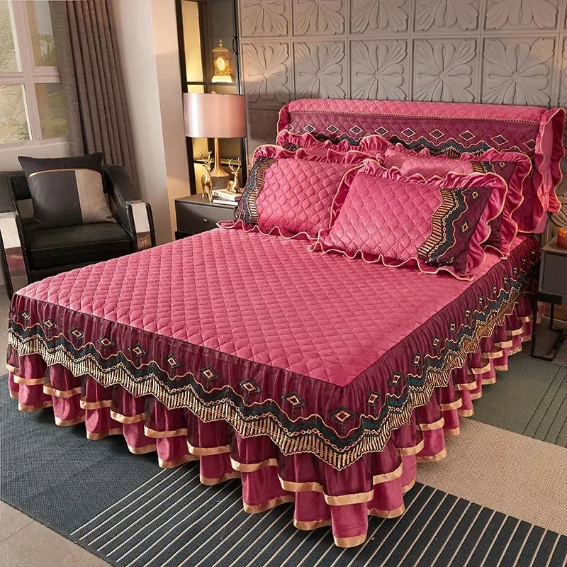 A pink quilted bed skirt with gold embroidery and ruffles is displayed on a bed.