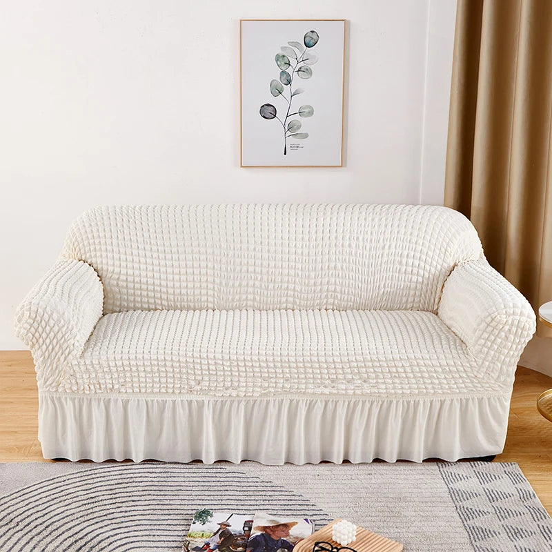 A cream-colored stretch knit sofa cover with a bubble lattice texture displayed on a wooden floor.