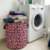 A white washing machine next to a pink leopard print laundry basket filled with dark clothing.