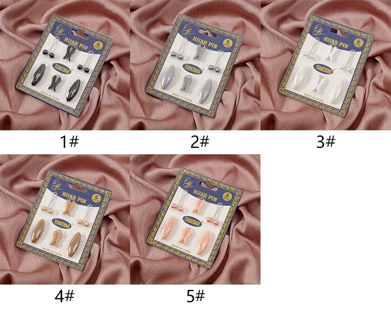 Five packaged sets of plastic safety pins for hijab accessories displayed on fabric.