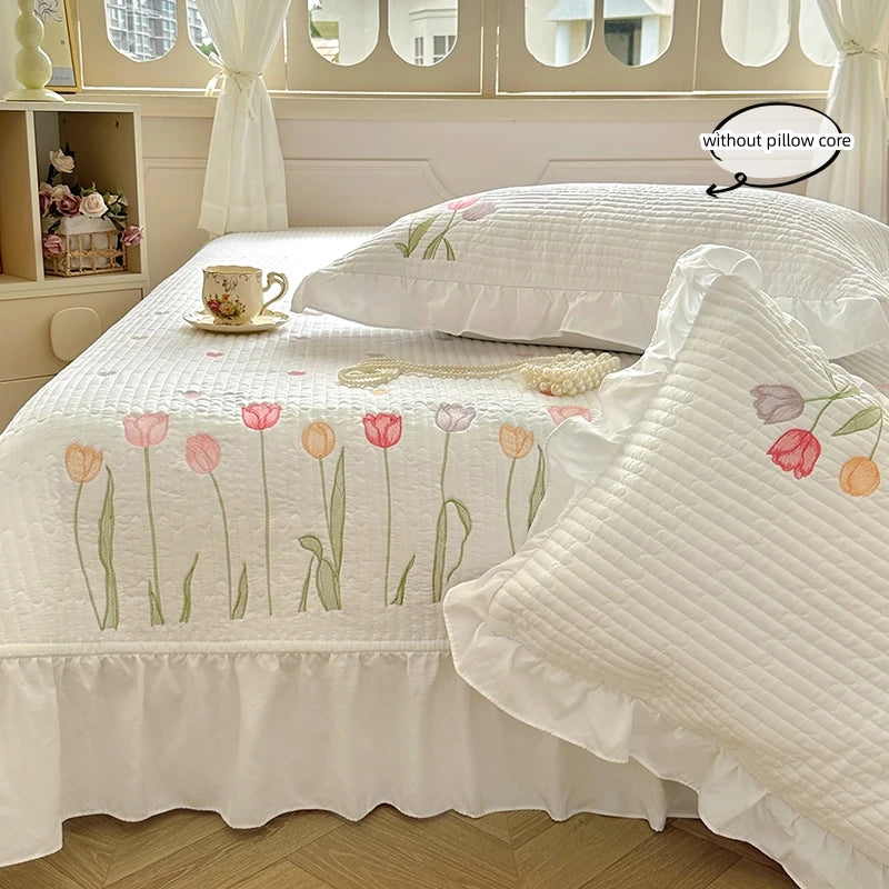 White quilted bedding set featuring embroidered pink and green floral designs on a bed.