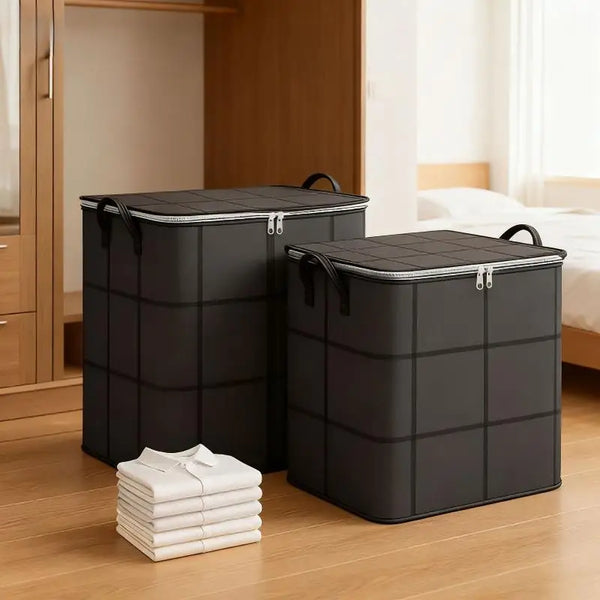 Two black storage bags with handles are placed on a wooden floor next to a stack of white folded clothes.