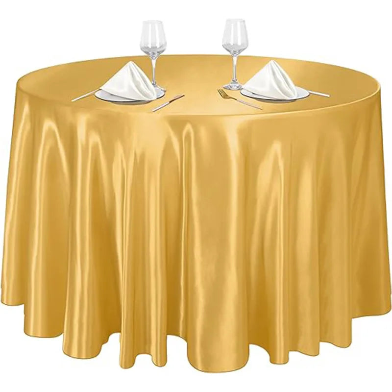 A round table set with a golden satin overlay cloth, white napkins, and silverware.