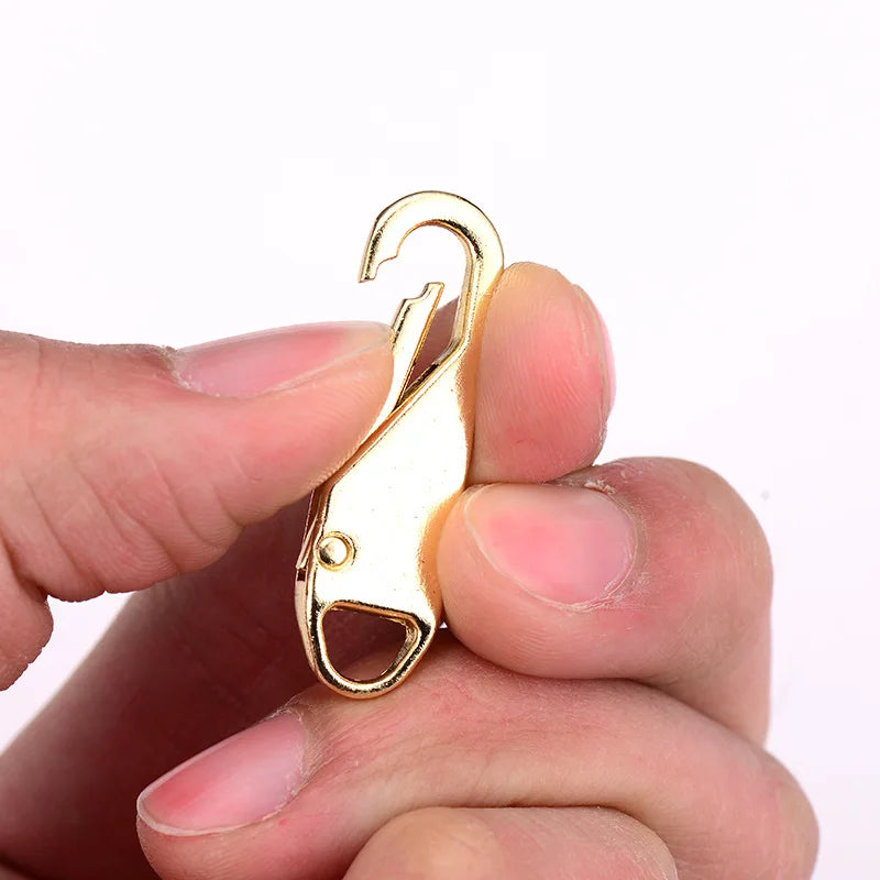 A hand holds a gold-colored zipper slider puller repair kit tool.