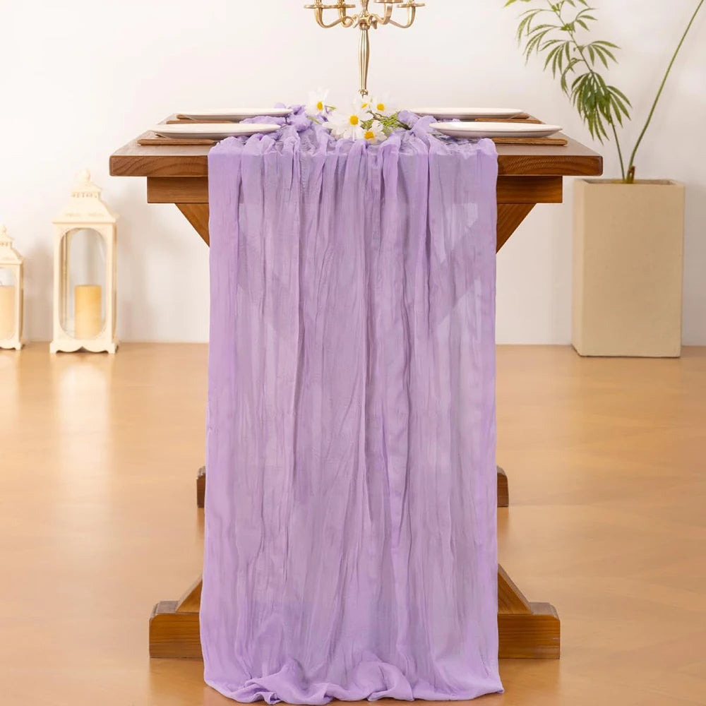 A purple cheesecloth table runner draped over a wooden table, decorated with flowers and a candelabra.