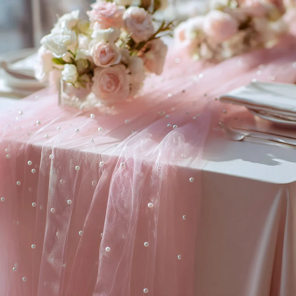 Pink pearl tulle table runner draped over a pink tablecloth with floral arrangements.