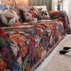 A richly colored floral jacquard sofa throw blanket draped over a sofa with patterned pillows.