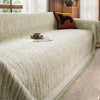 A light green textured sofa cover blanket draped over a sofa, with an orange dog pillow and wooden accents visible.