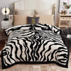 A black and white zebra patterned weighted blanket displayed on a bed with a white upholstered headboard.