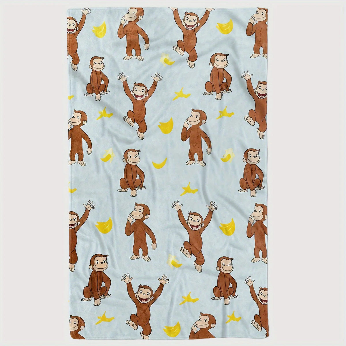 A light blue flannel throw blanket featuring illustrations of Curious George and yellow stars.