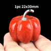 A bright red natural stone pumpkin figurine with a silver stem is held in a hand.