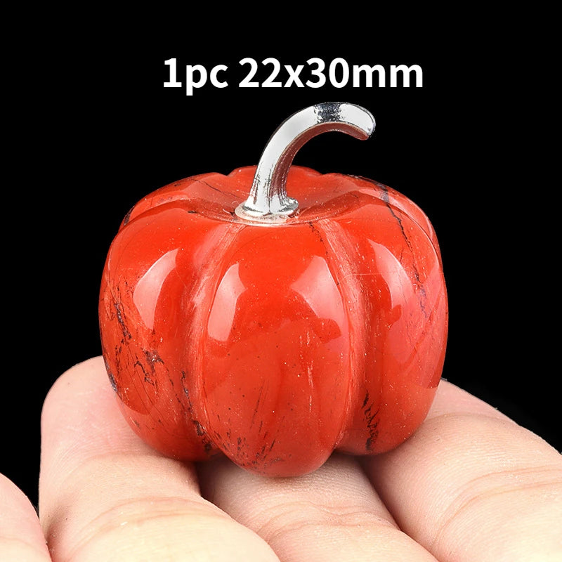 A bright red natural stone pumpkin figurine with a silver stem is held in a hand.