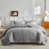 A light gray quilted duvet and pillow set displayed on a bed with white paneling and a wooden nightstand.