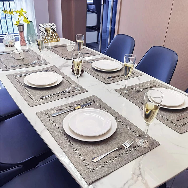 A white dining table set with linen placemats, silverware, and glassware in a modern interior setting.