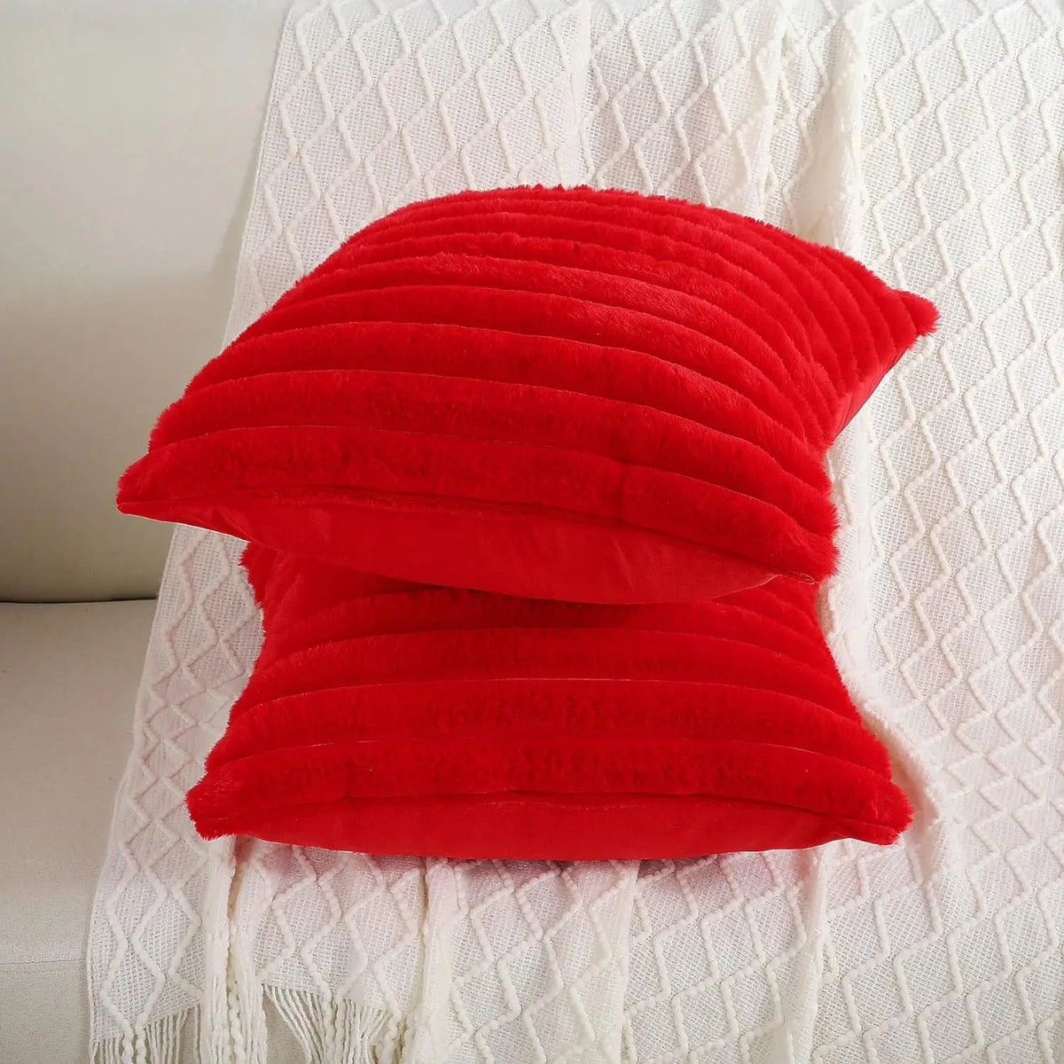 A stack of bright red, vertically ribbed faux rabbit fur cushion covers resting on a white textured fabric.