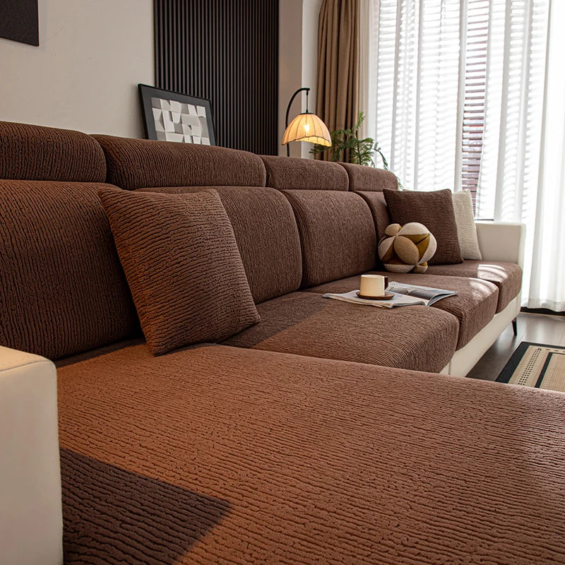 A brown stretch sofa seat cushion cover is shown on a sectional sofa in a bright room.