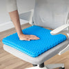 A hand rests on a blue honeycomb silicone seat cushion placed on a gray office chair.