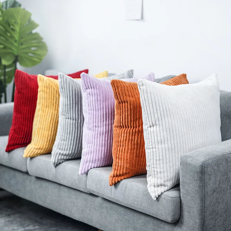 A row of colorful striped velvet corduroy cushion covers displayed on a gray sofa.
