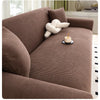 A brown stretch jacquard sofa slipcover with a textured fabric and a cream-colored decorative object on the seat.