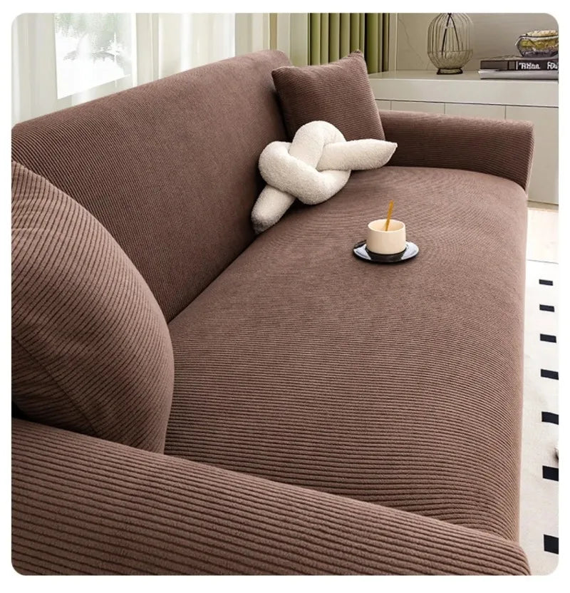 A brown stretch jacquard sofa slipcover with a textured fabric and a cream-colored decorative object on the seat.
