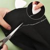 A hand uses scissors to remove chalk marks from black fabric, demonstrating erasable fabric chalk markers for sewing.
