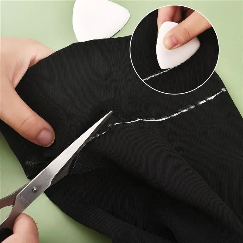 A hand uses scissors to remove chalk marks from black fabric, demonstrating erasable fabric chalk markers for sewing.