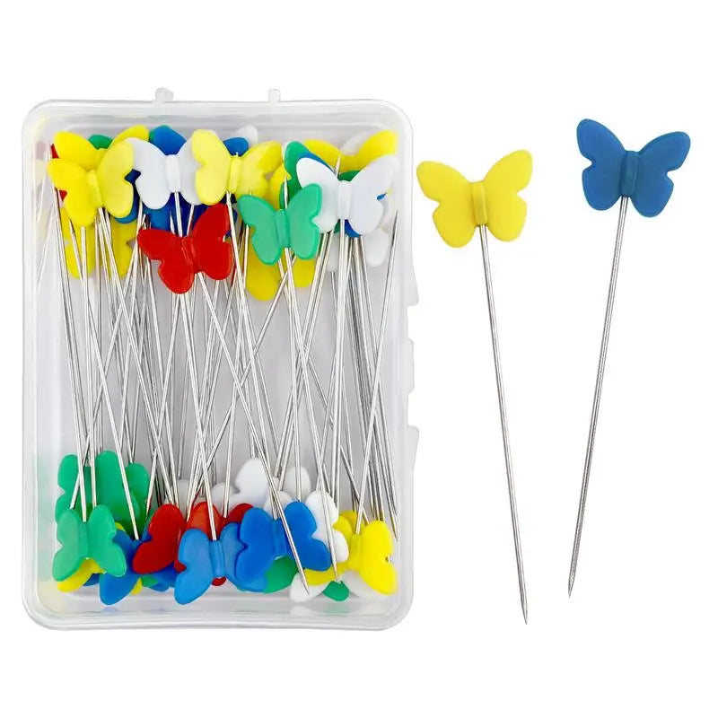 A clear plastic box containing dressmaking pins with colorful butterfly-shaped heads in yellow, blue, and red.