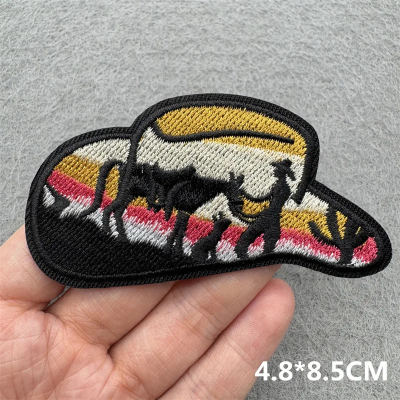 A black embroidered iron-on patch depicting a silhouette of a cowboy riding a horse against a striped background.