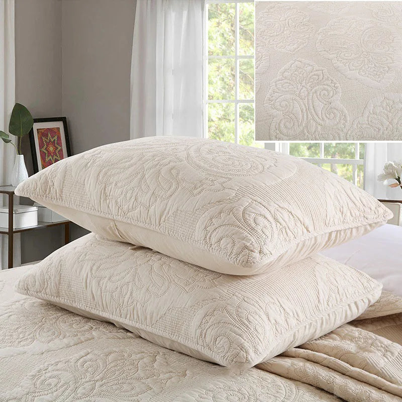 A set of cream embroidered cotton quilted pillows resting on a beige linen fabric.