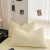A set of minimalist solid color duvet cover and pillowcases in a cream or off-white shade on a bed.