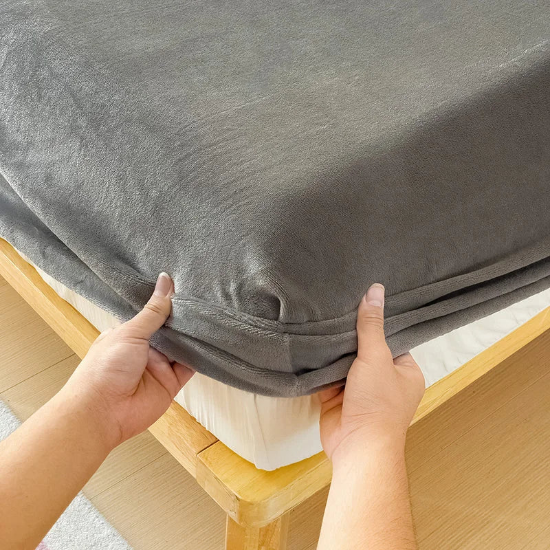 Hands are adjusting a gray flannel fitted sheet with deep pockets on a wooden bed frame.