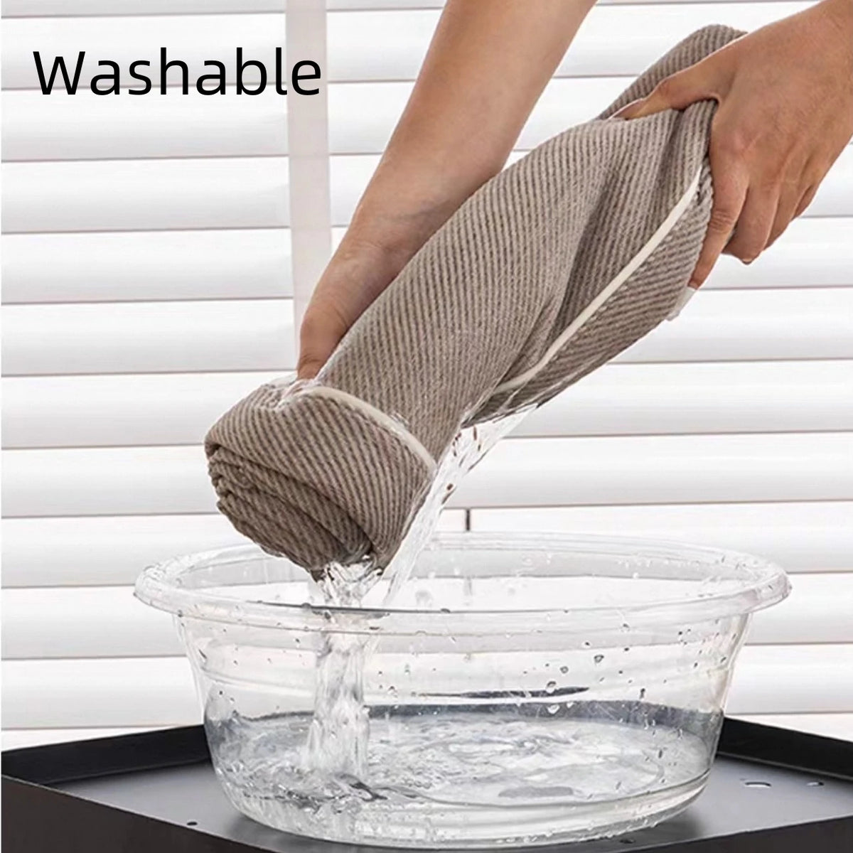 A hand is dipping a gray chenille sofa protector cover into a clear bowl of water for washing.